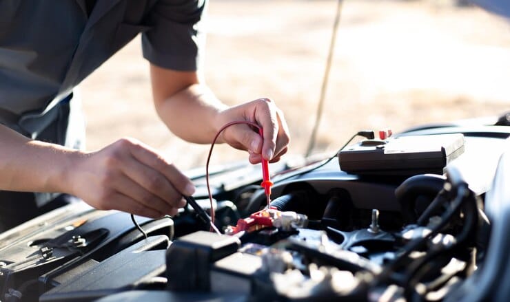 A man is engaged in car maintenance, handling a red wire in the engine compartment.